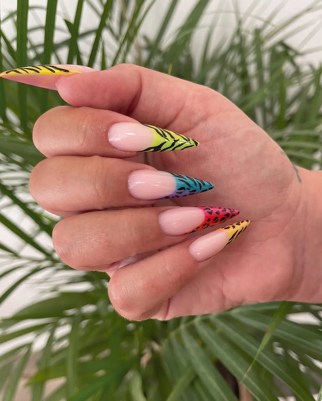 Uñas stiletto con diseño de cebra multicolor sobre fondo de plantas, trabajo de Manicuí